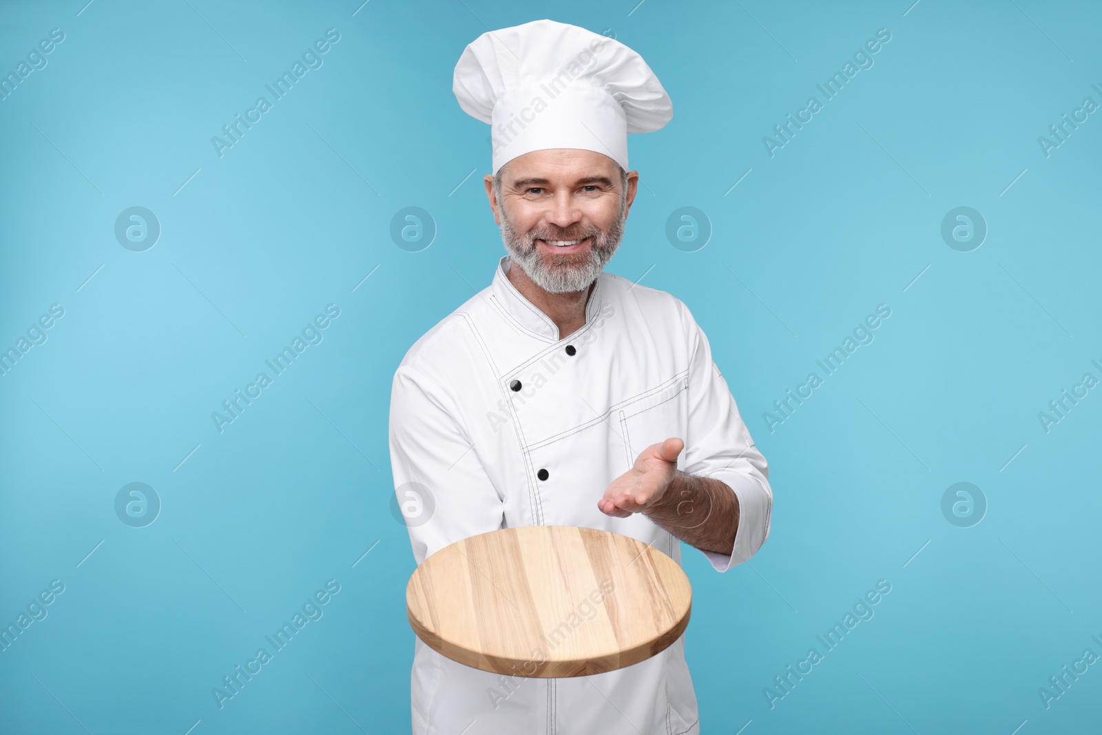 Photo of Happy chef in uniform showing wooden board on light blue background