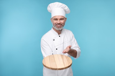 Happy chef in uniform showing wooden board on light blue background