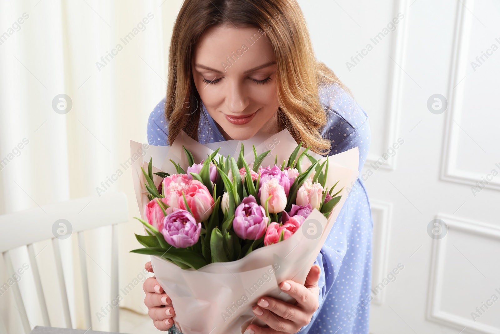 Photo of Happy young woman with bouquet of beautiful tulips indoors