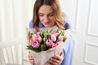 Happy young woman with bouquet of beautiful tulips indoors