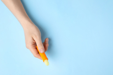 Woman holding hygienic lipstick on light blue background, top view. Space for text