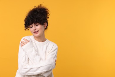 Happy young woman in stylish white sweater on yellow background, space for text