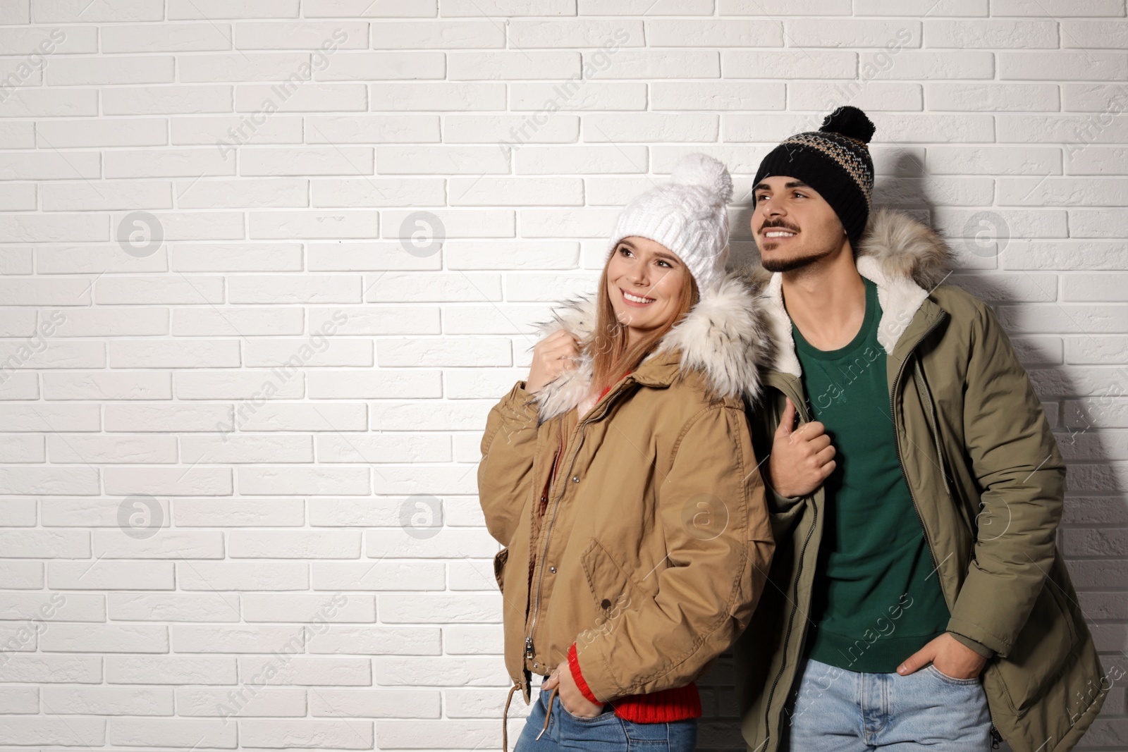 Photo of Young couple wearing warm clothes against brick wall, space for text. Ready for winter vacation