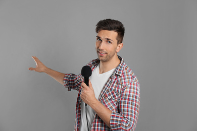 Young male journalist with microphone on grey background