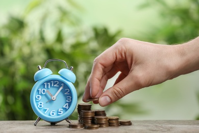 Woman stacking coins and light blue alarm clock on wooden table, closeup. Money savings