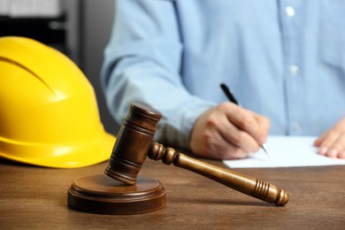 Photo of Construction and land law concepts. Man writing at wooden table, focus on gavel