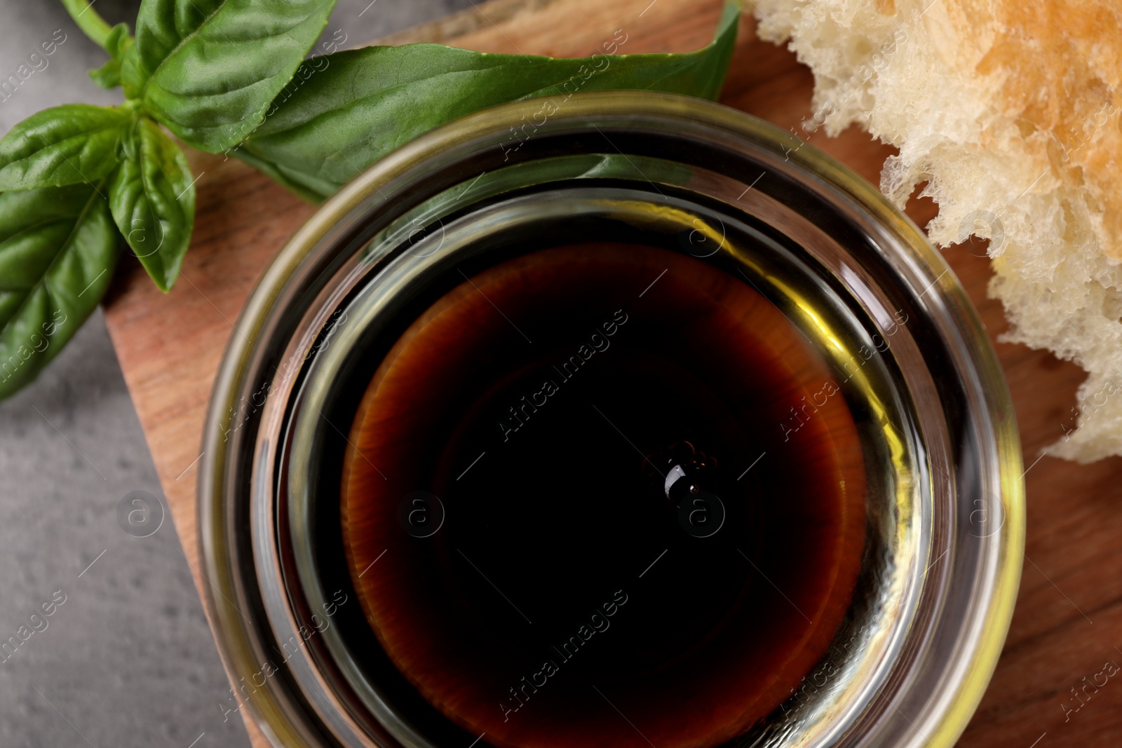 Photo of Bowl of organic balsamic vinegar with oil, basil and bread on grey table, flat lay