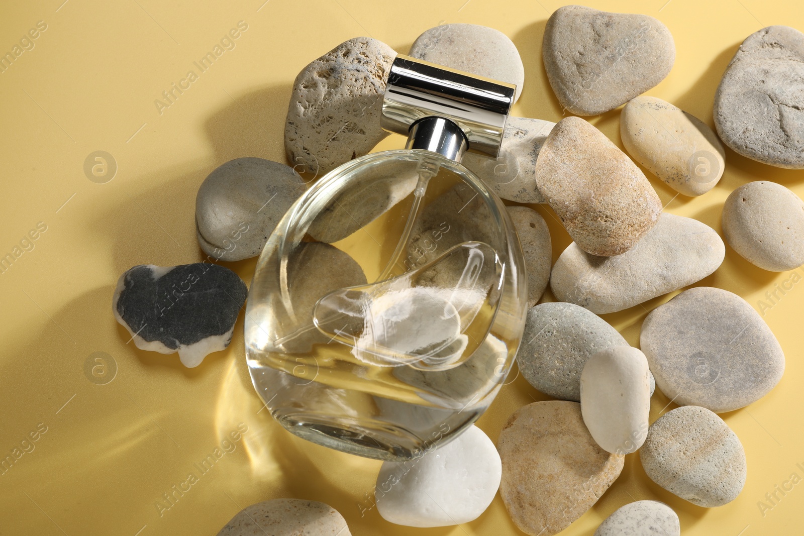 Photo of Bottle of luxury perfume in sunlight and stones on golden background, above view