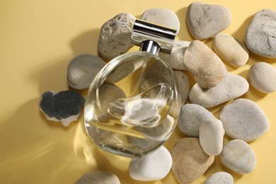 Bottle of luxury perfume in sunlight and stones on golden background, above view