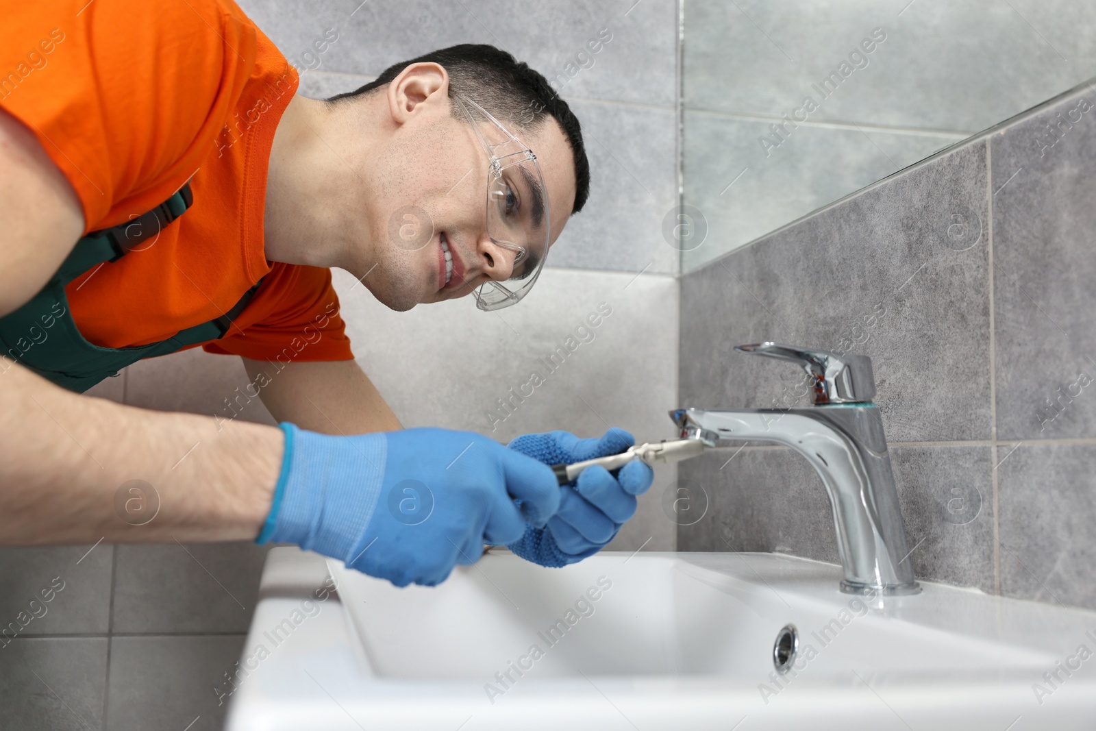 Photo of Smiling plumber repairing faucet with spanner in bathroom