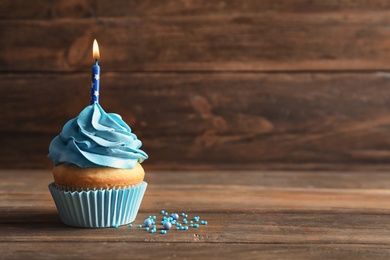 Photo of Delicious birthday cupcake with burning candle on wooden table