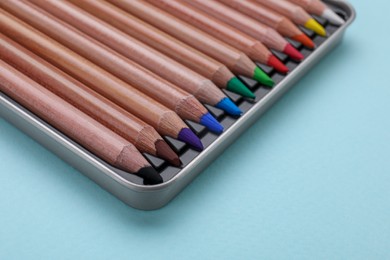 Photo of Colorful pastel pencils in box on light blue background, closeup. Drawing supplies