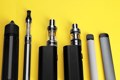 Photo of Different electronic cigarettes on yellow background, above view