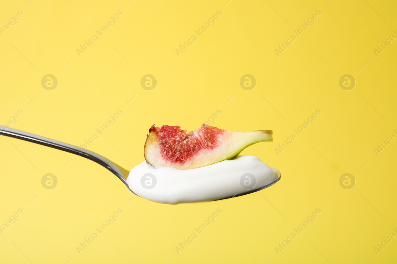 Photo of Spoon with yogurt and fig on yellow background, closeup