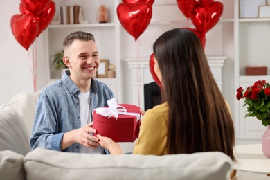 Photo of Man receiving gift box from his girlfriend at home. Valentine's day celebration