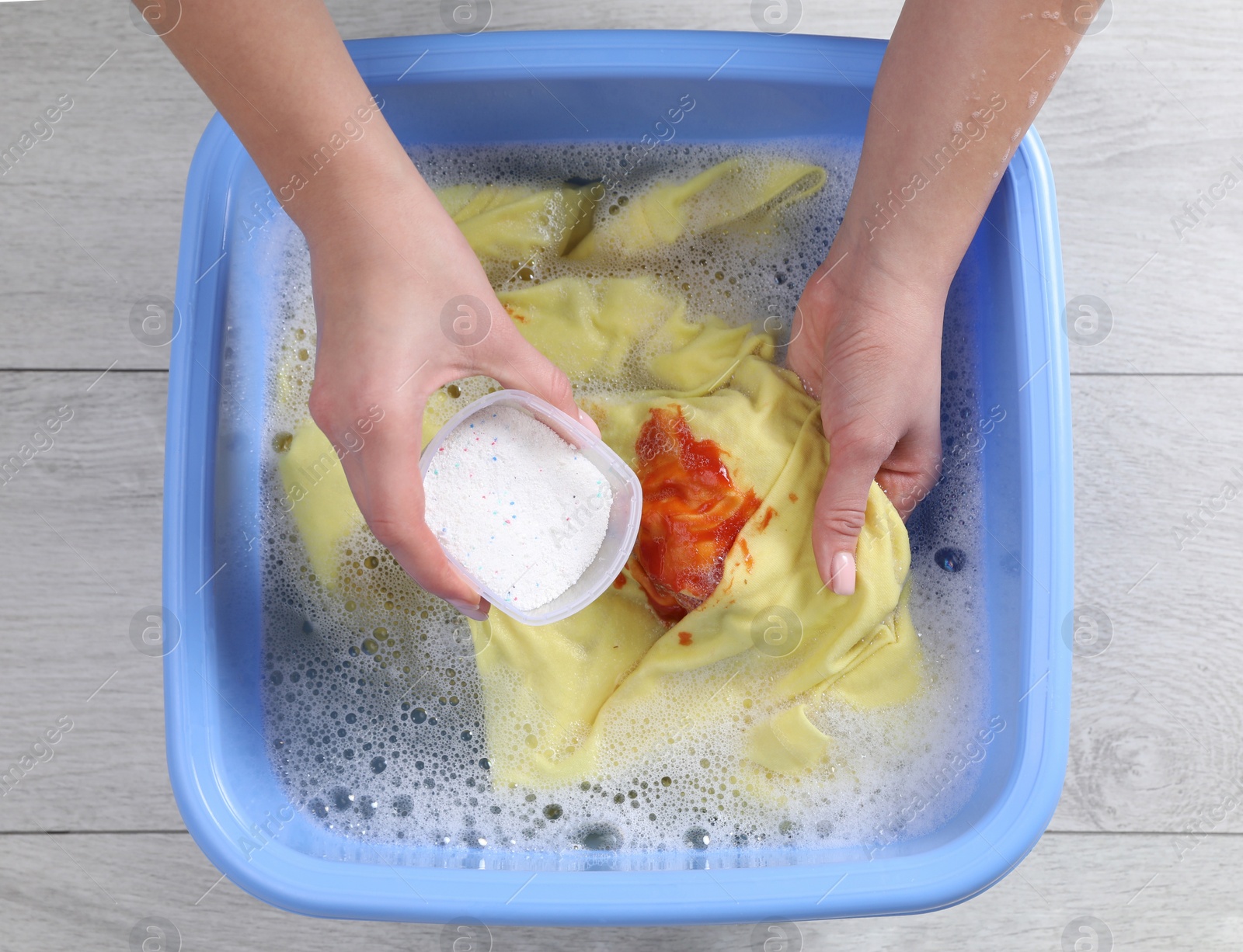 Photo of Woman adding powdered detergent into basin with clothes, top view. Hand washing laundry