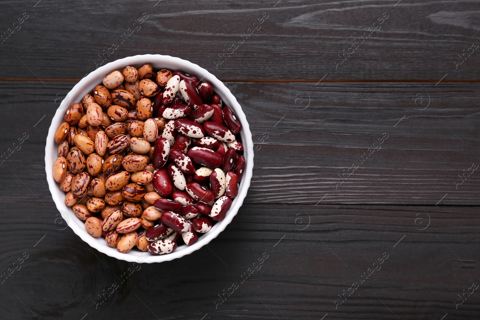 Photo of Different kinds of dry kidney beans in bowl on wooden table, top view. Space for text