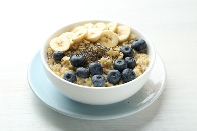 Photo of Tasty oatmeal with banana, blueberries and chia seeds served in bowl on white wooden table