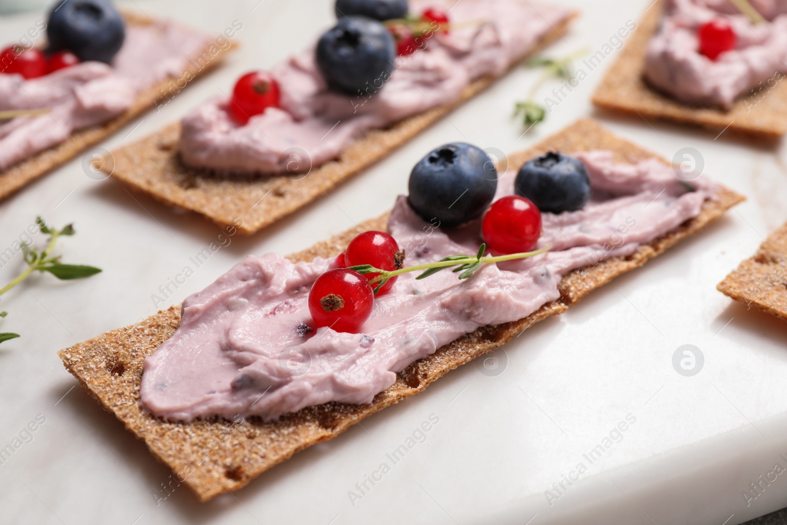 Photo of Tasty cracker sandwiches with cream cheese, blueberries, red currants and thyme on white board, closeup