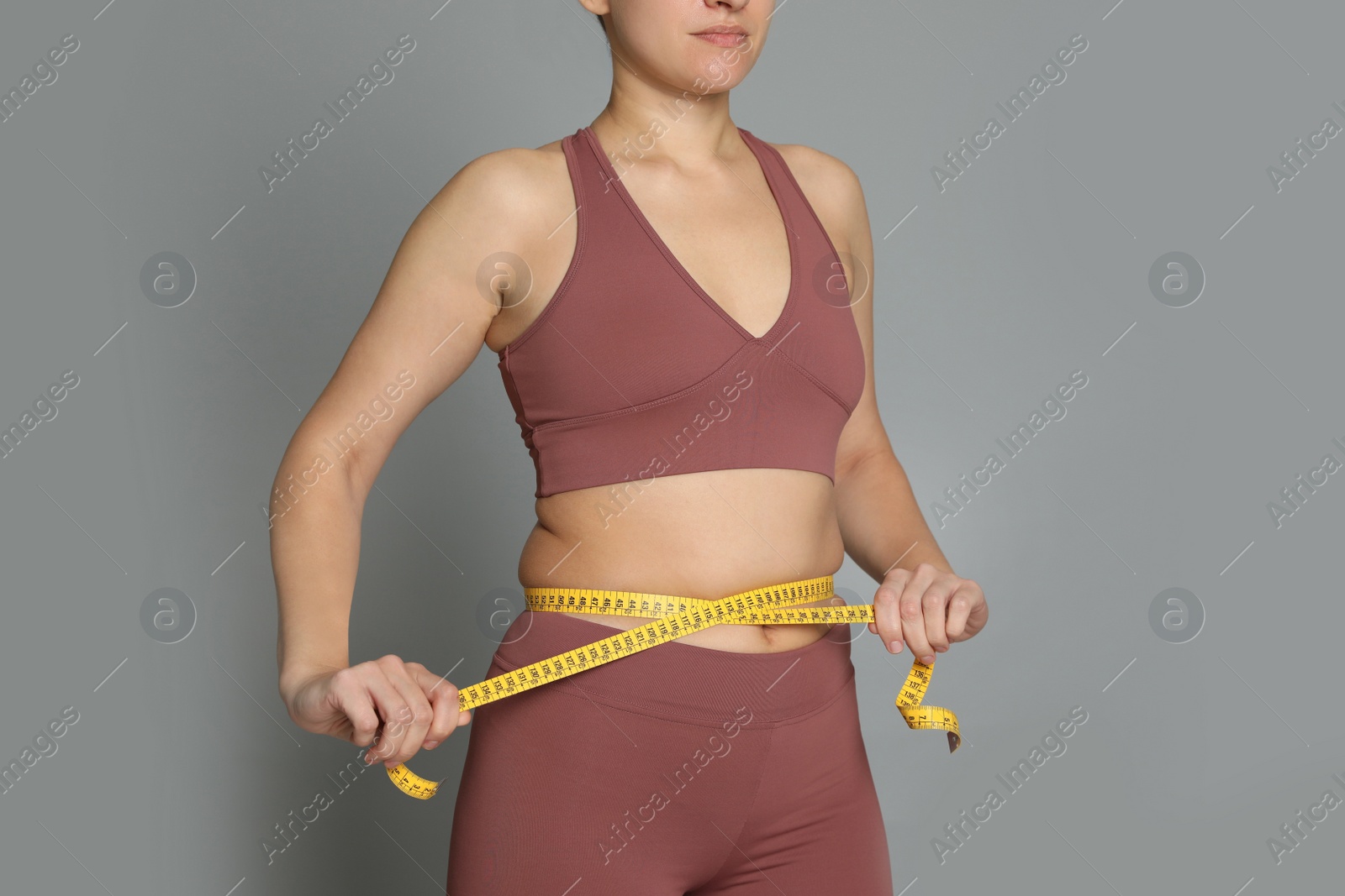 Photo of Woman measuring waist with tape on grey background, closeup