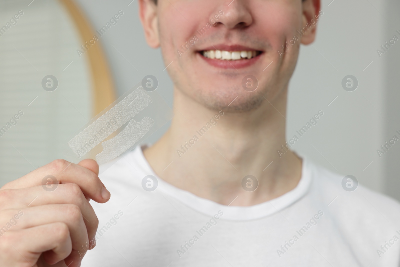 Photo of Young man with whitening strips indoors, closeup