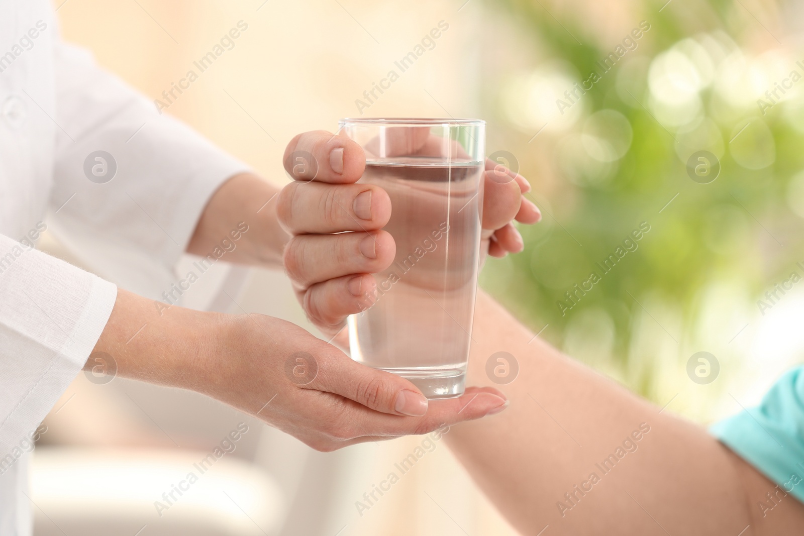 Photo of Nurse giving glass of water to elderly man indoors, closeup. Assisting senior generation