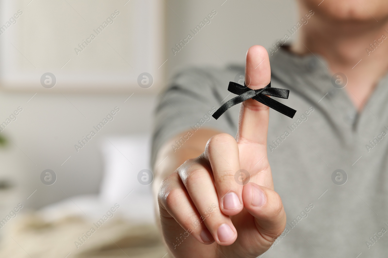 Photo of Man showing index finger with tied bow as reminder indoors, closeup. Space for text