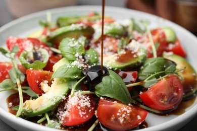 Pouring balsamic vinegar onto plate with tasty salad, closeup