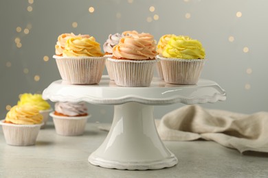 Photo of Dessert stand with tasty cupcakes on table against blurred lights