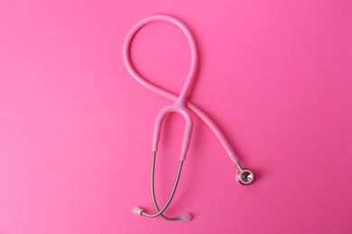 Photo of Pink stethoscope as awareness ribbon on color background, top view. Breast cancer concept