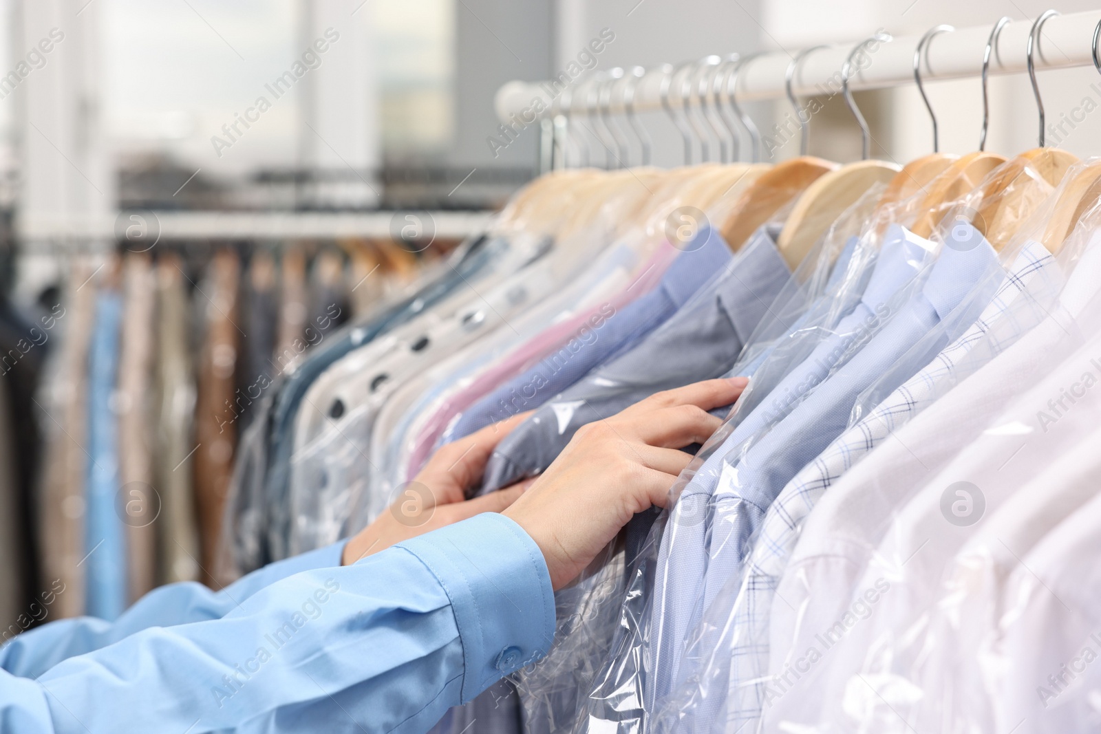 Photo of Dry-cleaning service. Woman taking shirt in plastic bag from rack indoors, closeup