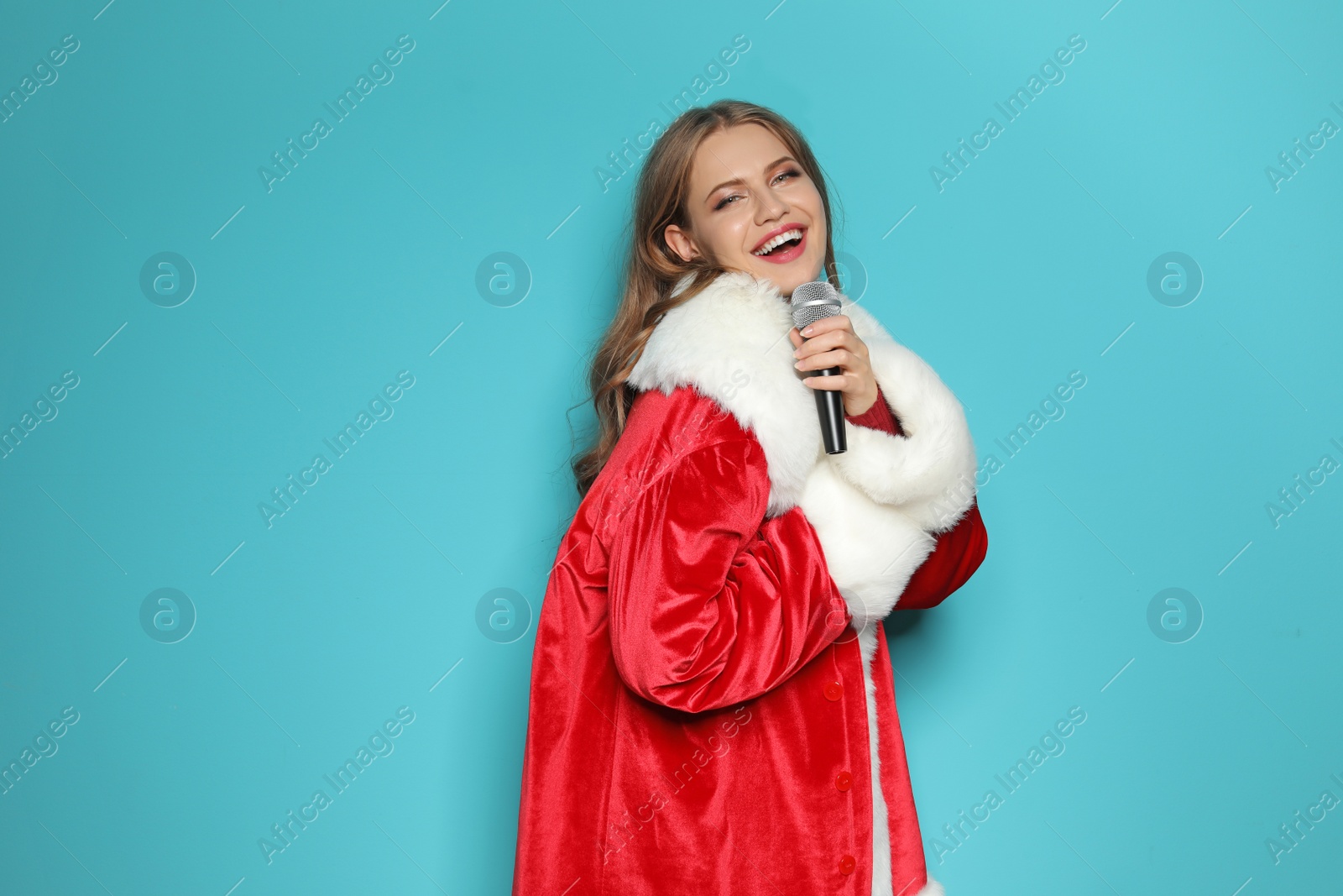 Photo of Young woman in Santa costume singing into microphone on color background. Christmas music