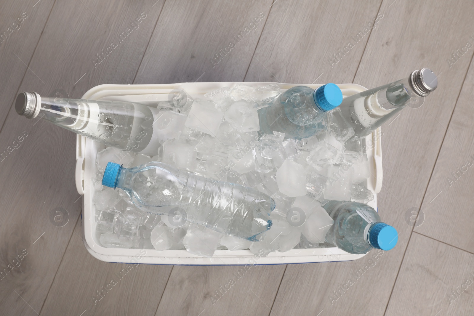 Photo of Plastic cool box with ice cubes and bottles of water on wooden floor, top view