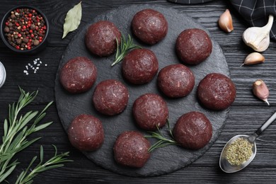 Many fresh raw meatballs and ingredients on black wooden table, flat lay