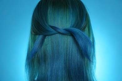 Woman with bright dyed hair on light blue background, back view