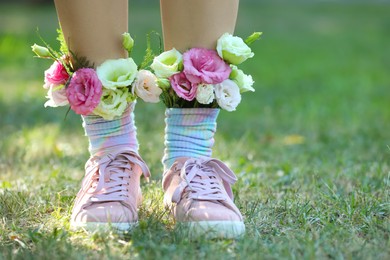 Photo of Woman standing on green grass with flowers in socks, closeup. Space for text
