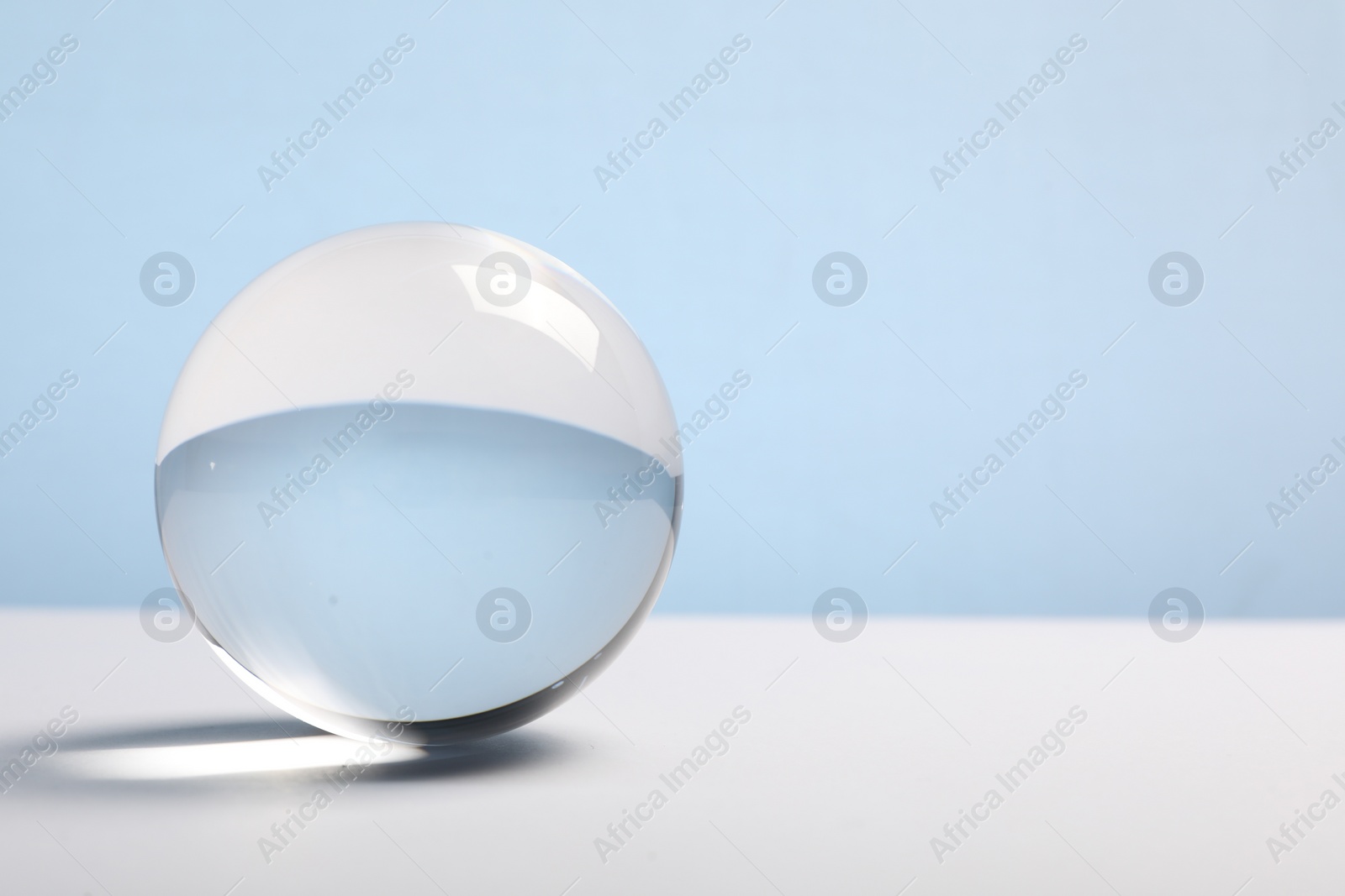 Photo of Transparent glass ball on table against light blue background. Space for text