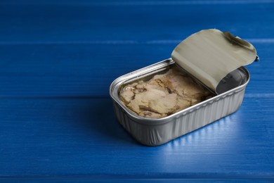 Open tin can of tasty cod liver on blue wooden table, closeup. Space for text