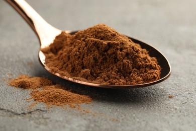 Photo of Spoon with cinnamon powder on grey table, closeup