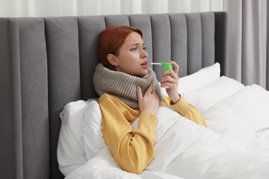 Photo of Young woman with scarf using throat spray in bed