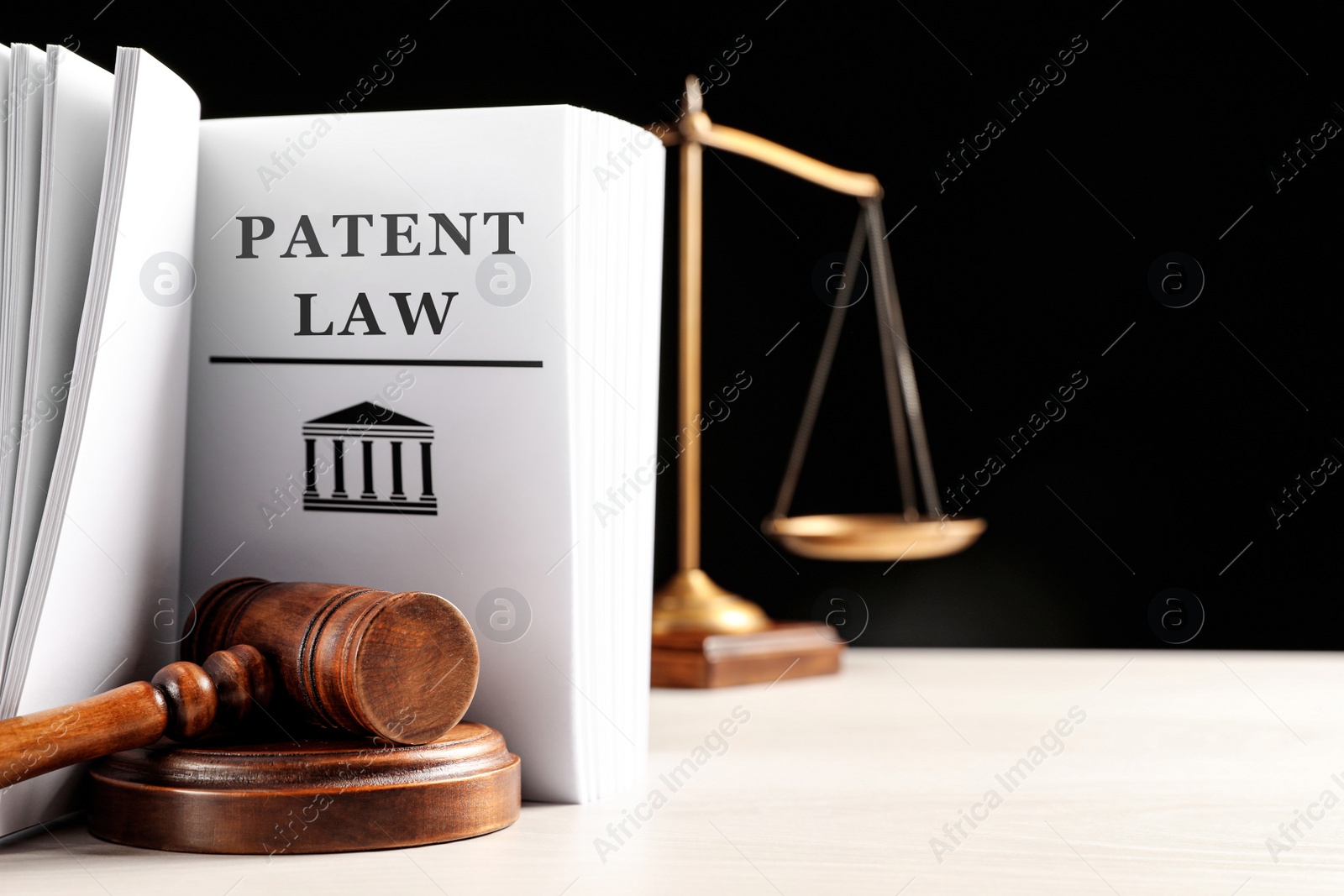 Image of Judge's gavel, Patent Law book and scales on white table against black background. Space for text