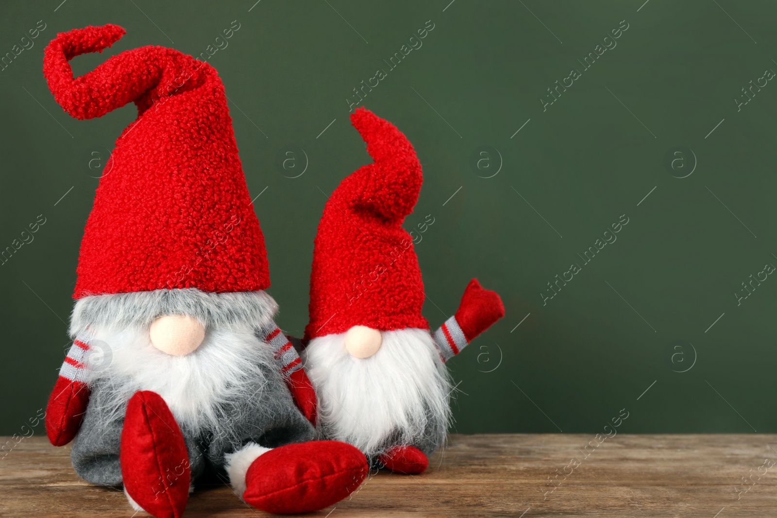 Photo of Cute Christmas gnomes on wooden table against green background. Space for text