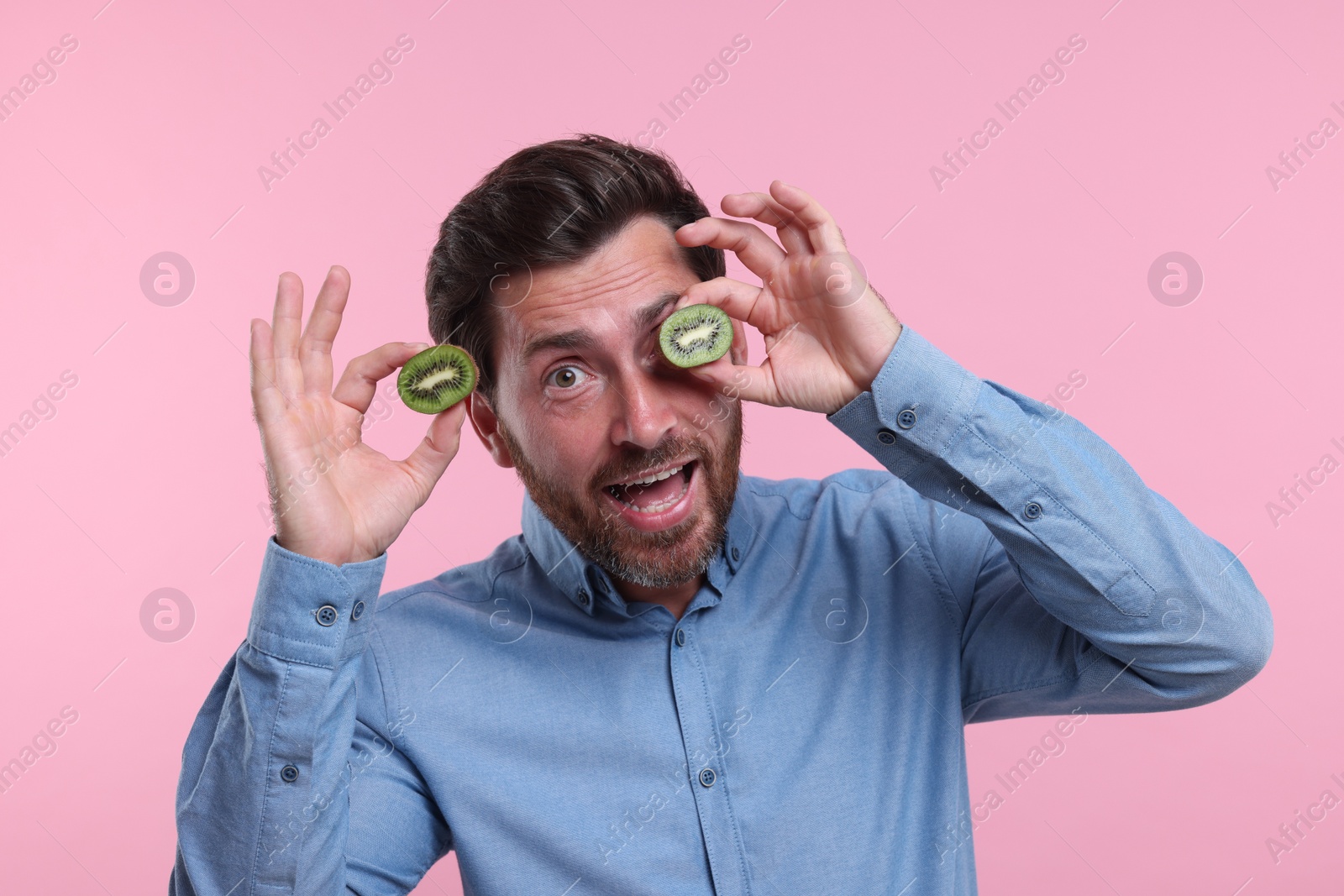 Photo of Emotional man holding halves of kiwi on pink background