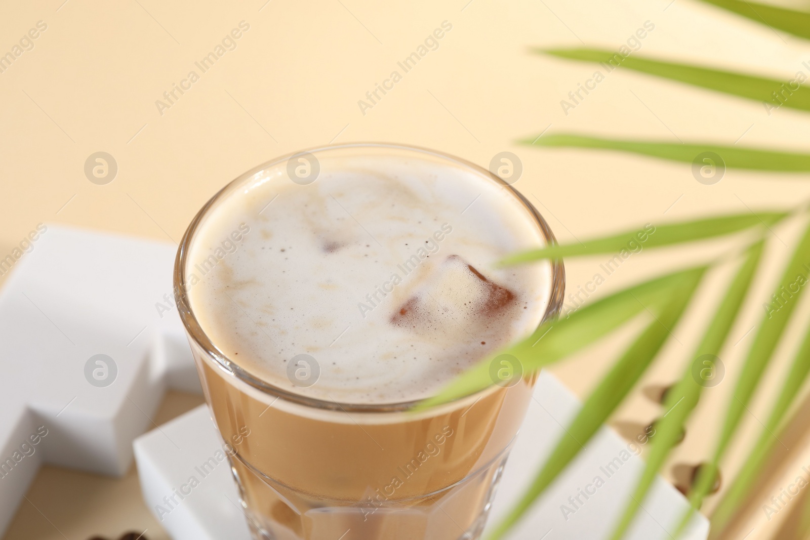 Photo of Refreshing iced coffee with milk in glass on pale yellow table, closeup