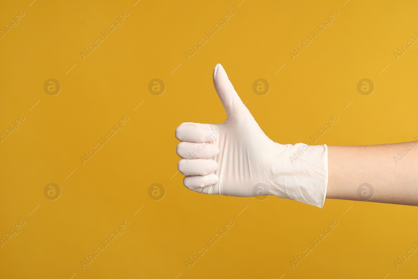 Photo of Doctor in medical gloves showing thumb up on yellow background, closeup. Space for text