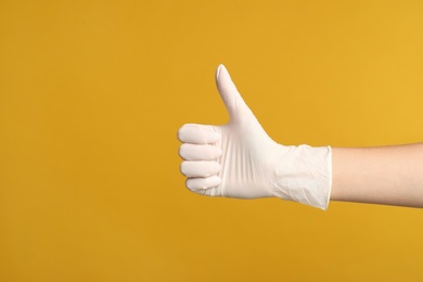 Photo of Doctor in medical gloves showing thumb up on yellow background, closeup. Space for text