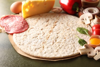 Pizza base and products on green textured table, closeup