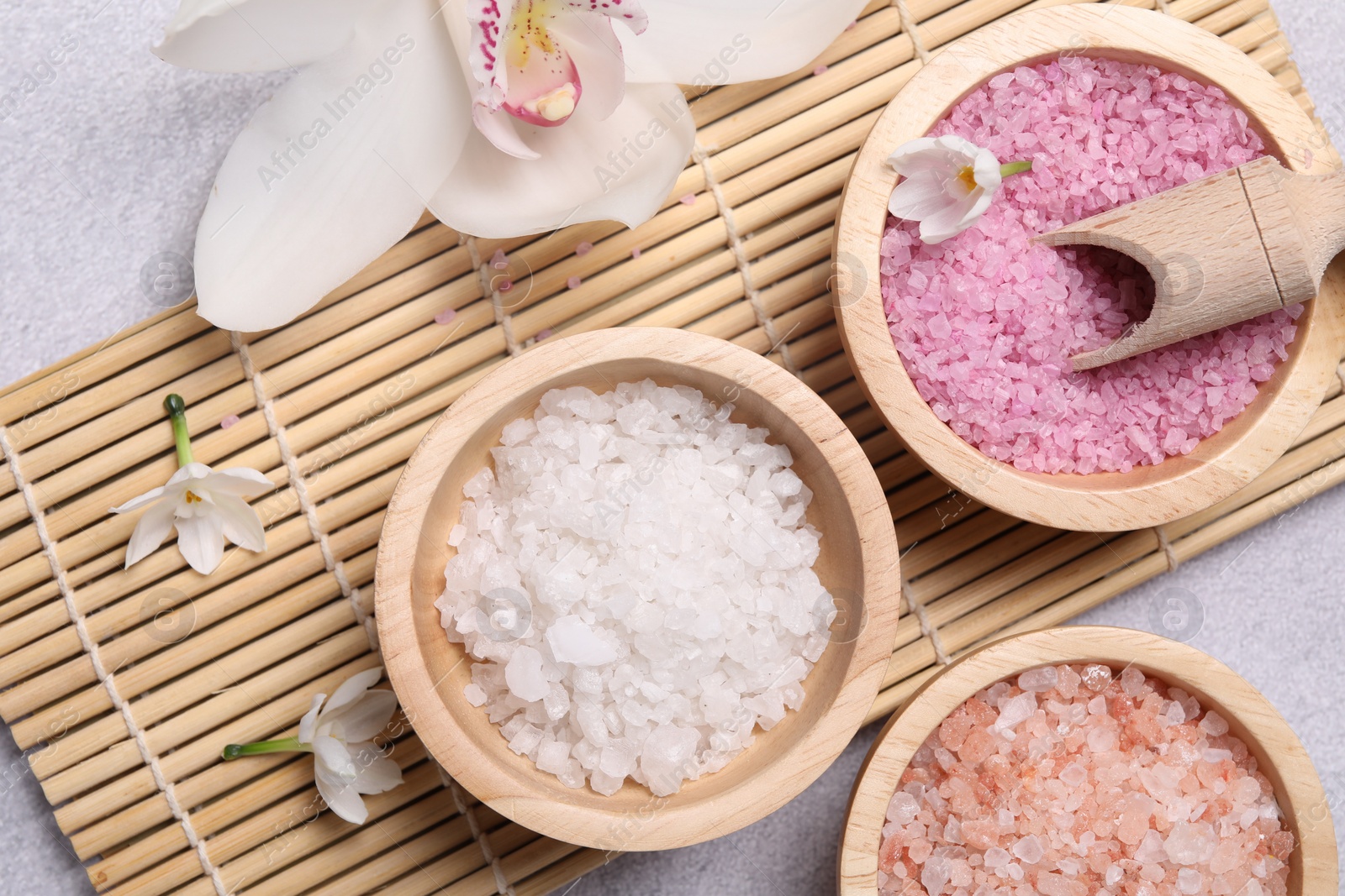 Photo of Different types of sea salt and flowers on light table, flat lay. Spa products