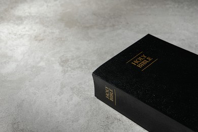 Bible with black cover on light gray table, space for text. Christian religious book