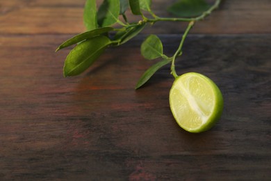 Branch with fresh leaves and lime on wooden table, closeup. Space for text